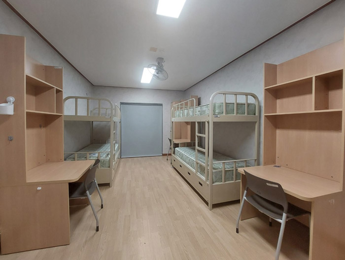 3인실을 정면에서 바라 본 모습으로 좌우에는 책상과 그 옆은 2층침대가 있으며, 머리맡에는 창물과 블라인드가 설치되어 있다.